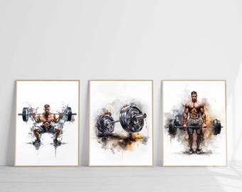 May include: Set of three framed watercolor prints featuring weightlifting themes. The prints depict a person lifting a barbell, a barbell with weights, and a person lifting a barbell. The artwork has a watercolor effect with splashes of color.