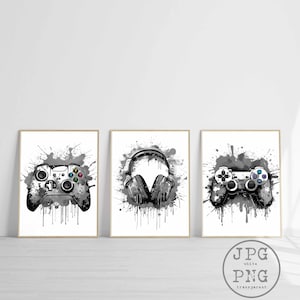 May include: Three black and white illustrations of gaming accessories. The first illustration is a video game controller with paint splatters. The second illustration is a pair of headphones with paint splatters. The third illustration is a video game controller with paint splatters.