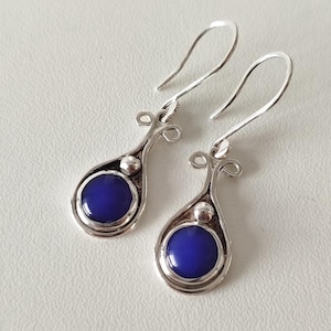 May include: A pair of silver dangle earrings with blue round stones. The earrings have a delicate, ornate design.