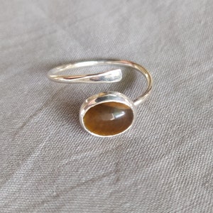 May include: A silver ring with a brown tiger's eye stone. The ring is open and adjustable.