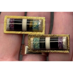 May include: A pair of rectangular cufflinks featuring a gold-toned textured frame surrounding a horizontal inlay of multi-colored stone segments, including purple, black, white, brown, and green patterned minerals.