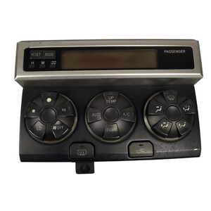 May include: A black and silver automotive climate control unit featuring a digital display screen, three circular control dials with various settings, and buttons labeled RESET, MODE, H, M, :00, PASSENGER, UP, TEMP, AUTO, A/C, DOWN, HI, LO, OFF, and icons for defrost.