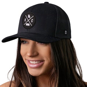 May include: Black trucker hat with a black and white patch featuring the letters "KC" with a cross and the outline of the state of Missouri.