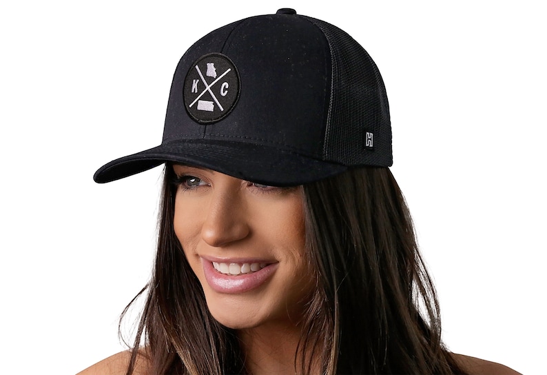 May include: Black trucker hat with a black and white patch featuring the letters "KC" with a cross and the outline of the state of Missouri.