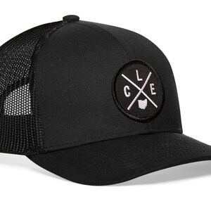 May include: Black trucker hat with a black and white circular patch that says "CLE" with a white "X" and a white outline of the state of Ohio.