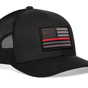 May include: Black trucker hat with a red line American flag patch. The hat has a mesh back.