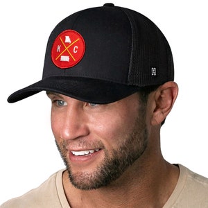 K&ouml;nnte beinhalten: Schwarze Trucker-Cap mit gebogenem Schirm und Mesh-R&uuml;ckseite. Auf der Vorderseite befindet sich ein kreisf&ouml;rmiger Aufn&auml;her mit rotem Hintergrund, den Buchstaben "K" und "C" sowie den Umrissen von Missouri und Kansas.