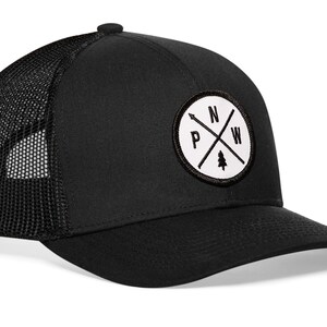 May include: Black mesh trucker hat with a white circular patch featuring a compass design with the letters "N", "W", "P", and "S" and a small pine tree graphic.