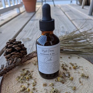 May include: A brown glass bottle with a dropper top and a white label that reads "Myste Dreamy Apothecary & Art Calm A Chamomile Tincture that soothes the mind, eases tension and promotes restful sleep".