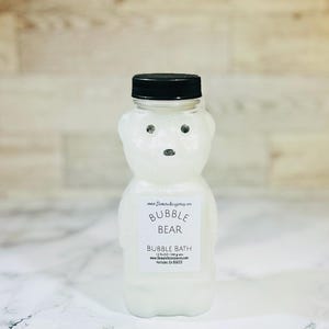 May include: A white plastic bear-shaped bottle filled with bubble bath. The bottle has a black lid and a label that reads "Bubble Bear Bubble Bath 12 fl oz / 340 grams www.DomtekiAccessories.com Hollister, CA 95023".