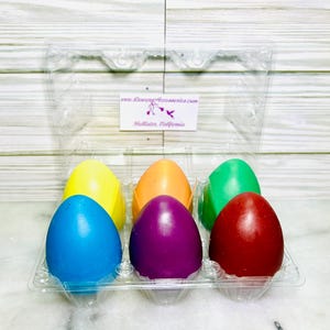 May include: Six colorful wax eggs in a clear plastic egg carton. The eggs are yellow, orange, green, blue, purple, and red.