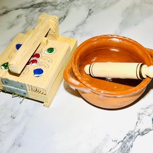 May include: A wooden tortilla press with a painted floral design and a terracotta bowl with a rolling pin inside.