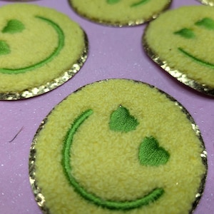 May include: Yellow smiley face patches with green eyes and a green smile. The patches have a gold glitter trim.
