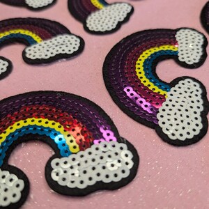 Puede incluir: Un conjunto de parches de lentejuelas de colores arcoíris con un diseño de nube blanca. Los parches son perfectos para agregar un toque de fantasía a la ropa, los bolsos u otros accesorios.