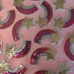 Könnte beinhalten: Eine Sammlung von regenbogenförmigen und sternförmigen Bügelbildern. Die Patches bestehen aus Pailletten in den Farben Pink, Rot, Silber und Gold.