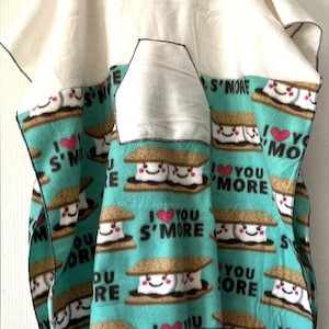 May include: A turquoise fleece blanket with a pattern of smiling s'mores and the text "I love you s'more". The blanket has a white fleece pocket on the front.