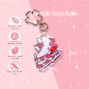 May include: White ice skate with pink cherry blossoms printed on a clear acrylic keychain. The keychain is 2 inches tall and has a gold metal clasp.