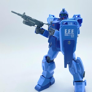May include: A blue and gray plastic action figure of a robot holding a gun. The robot has a shield on its left arm with the text "E.F.F. 01" on it.