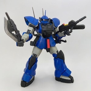 May include: A blue and gray robot action figure with a black chest and red accents. The robot is holding a large axe in one hand and a black rifle in the other. The figure has a detailed design and is posed in a dynamic stance.