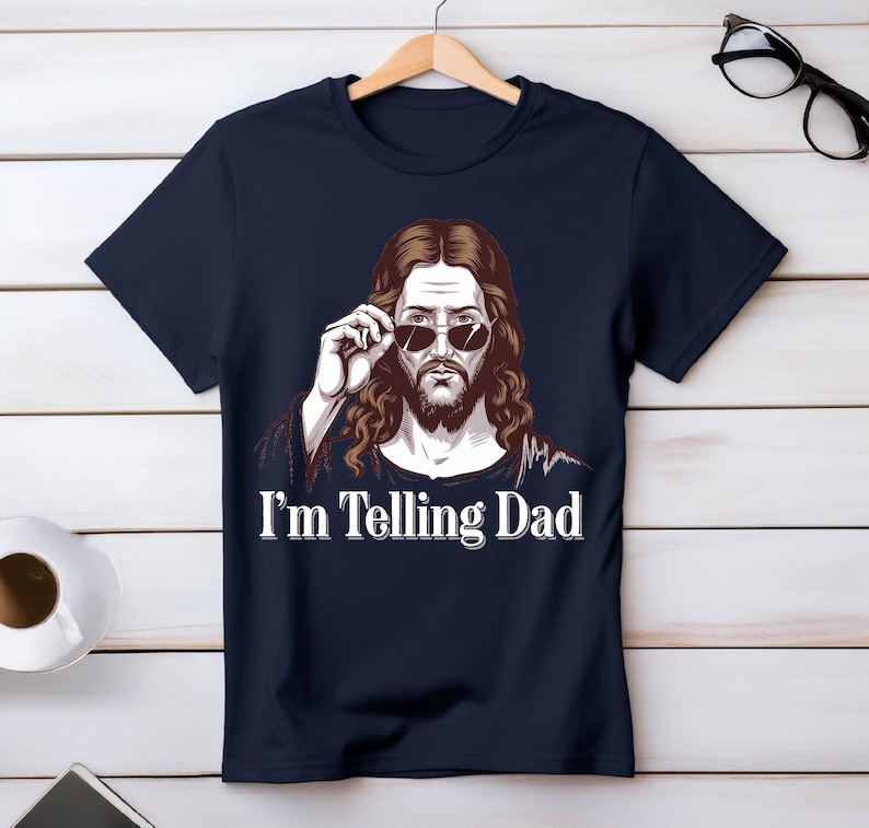 May include: A navy blue t-shirt with a graphic of Jesus wearing sunglasses and the text "I'm Telling Dad".