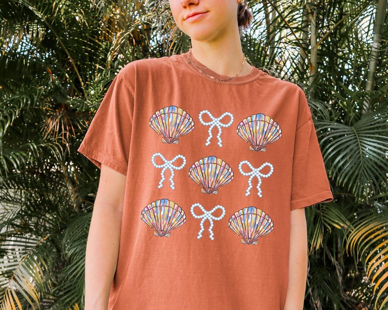 Comfort Colors t-shirt with a seashell and bow design, perfect for beach days, coastal vibes, and summer outings with a preppy aesthetic