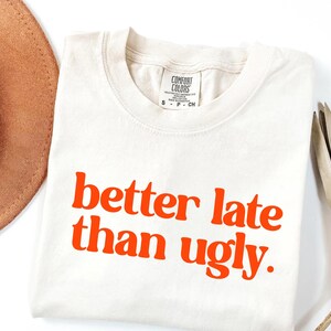 T-shirt with bold orange text that reads better late than ugly in playful retro-style font