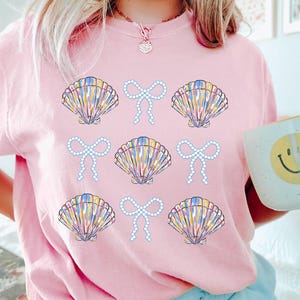 Comfort Colors t-shirt with a seashell and bow design, perfect for beach days, coastal vibes, and summer outings with a preppy aesthetic