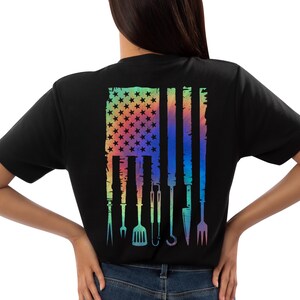 T-shirt featuring a rainbow American flag design made of BBQ grilling tools like tongs, spatula, and fork