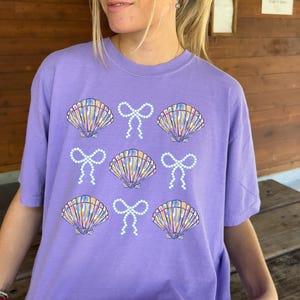Comfort Colors t-shirt with a seashell and bow design, perfect for beach days, coastal vibes, and summer outings with a preppy aesthetic