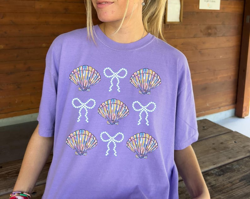 Comfort Colors t-shirt with a seashell and bow design, perfect for beach days, coastal vibes, and summer outings with a preppy aesthetic