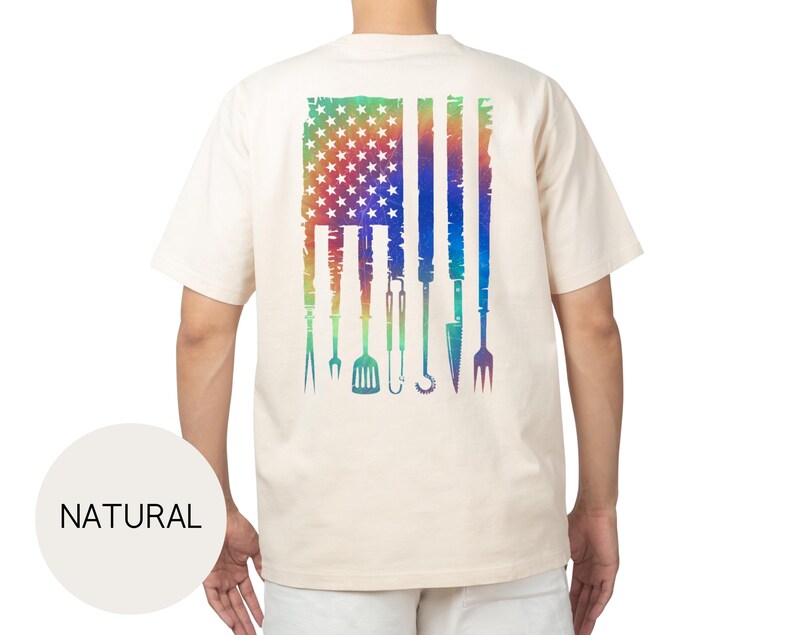 May include: A natural-colored t-shirt featuring a distressed American flag design on the back. The flag is rendered in a rainbow gradient, with grilling tools replacing the stripes. The word "NATURAL" is printed on a circular label.