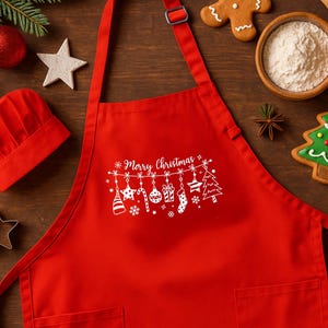May include: A bright red apron featuring a white graphic print of hanging Christmas ornaments, a candy cane, a stocking, and a tree, with the text Merry Christmas centered above the decorations. The apron includes a neck strap and two pockets.