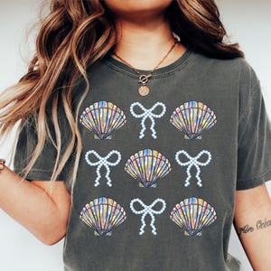 Comfort Colors t-shirt with a seashell and bow design, perfect for beach days, coastal vibes, and summer outings with a preppy aesthetic