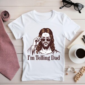 May include: White t-shirt with a drawing of Jesus wearing sunglasses and the text "I'm Telling Dad".