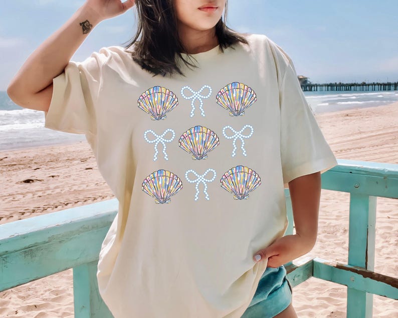 Comfort Colors t-shirt with a seashell and bow design, perfect for beach days, coastal vibes, and summer outings with a preppy aesthetic