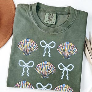 Comfort Colors t-shirt with a seashell and bow design, perfect for beach days, coastal vibes, and summer outings with a preppy aesthetic