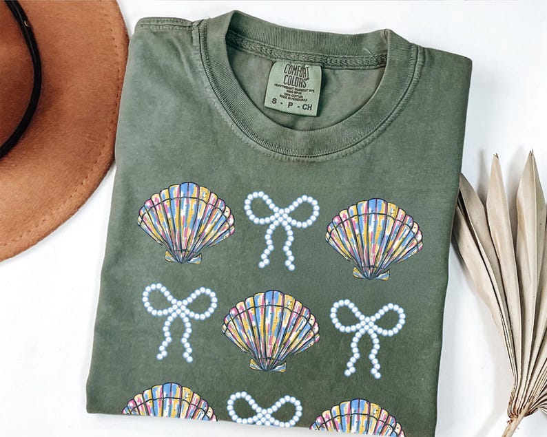 Comfort Colors t-shirt with a seashell and bow design, perfect for beach days, coastal vibes, and summer outings with a preppy aesthetic
