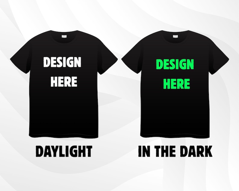 May include: Two black t-shirts with the text "DESIGN HERE" in white and green. The text "DAYLIGHT" is below the white text, and "IN THE DARK" is below the green text. The shirts are displayed on a white and grey gradient background.