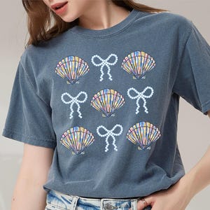 Comfort Colors t-shirt with a seashell and bow design, perfect for beach days, coastal vibes, and summer outings with a preppy aesthetic