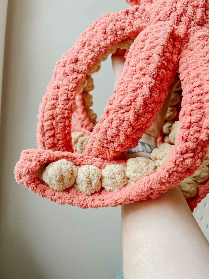 May include: A crocheted octopus toy with pink and beige yarn. The octopus has eight tentacles and a round head with a textured surface.