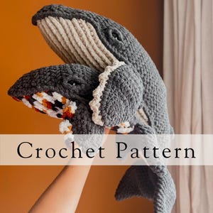May include: Crochet pattern for a grey and white whale amigurumi. The whale is holding a smaller grey whale amigurumi with orange and white stripes.