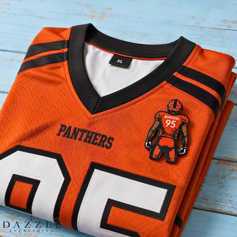 May include: An orange V-neck sports jersey with black trim and white accents. The word PANTHERS is printed in black on the chest. A graphic of a football player with the name BURGESS and number 95 is attached. The jersey has an XL size tag.