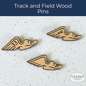 Peut inclure: Trois épingles en bois en forme de chaussures de course ailées. Les épingles sont de couleur beige avec des contours noirs et portent les chiffres "33" et "7" et le mot "LANE". Le texte "Track and Field Wood Pins" est en haut.