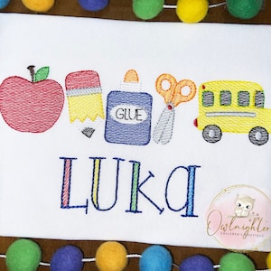 May include: A white t-shirt with an embroidered design of a red apple, yellow pencil, blue glue bottle, silver scissors, and a yellow school bus. The name "Luka" is embroidered below the design.