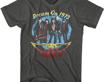 May include: A dark grey t-shirt featuring a vintage-style graphic of the band Aerosmith. The graphic shows the band members in a circle with the text "Dream On 1973" above them. The Aerosmith logo is below the band members.