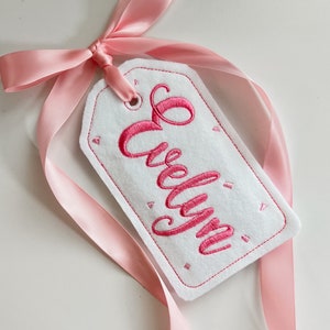 May include: A white felt gift tag with pink ribbon and the name "Evelyn" embroidered in pink cursive lettering.