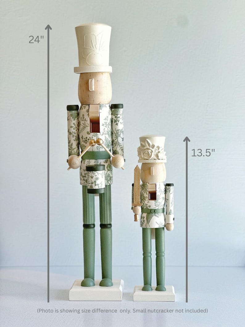 May include: Two decorative wooden nutcrackers. The larger one is 61 cm tall, and the smaller one is 34 cm tall. Both have a light wood head and a white hat. The bodies are decorated with a green and white floral pattern. The legs are green.