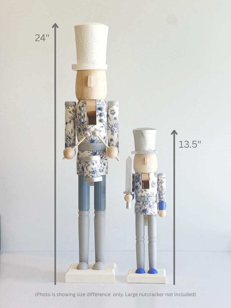 May include: Two wooden nutcrackers, one 24 inches tall and the other 13.5 inches tall. Both have a light wood head and a white hat. The bodies are decorated with a blue floral pattern. One holds drumsticks, the other a sword.
