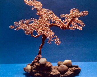 May include: A copper wire bonsai tree sculpture with a brown rock base and small stones. The tree is made of coiled wire and has a natural, organic look.