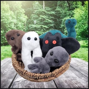 Puede incluir: Una cesta de mimbre llena de varios peluches de diferentes colores. Los juguetes incluyen una criatura marrón, una figura blanca, una criatura negra con ojos rojos, una criatura gris y un juguete con forma de dinosaurio verde azulado. El fondo es una escena exterior borrosa.